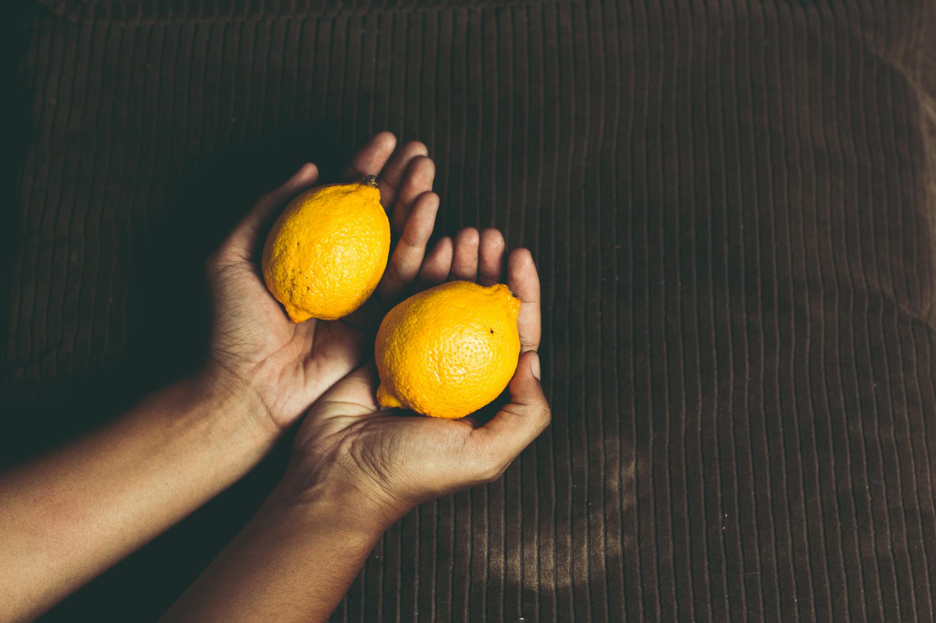 Due limoni freschi stretti in mani coperte, su una superficie marrone, simbolo di freschezza e vitalità