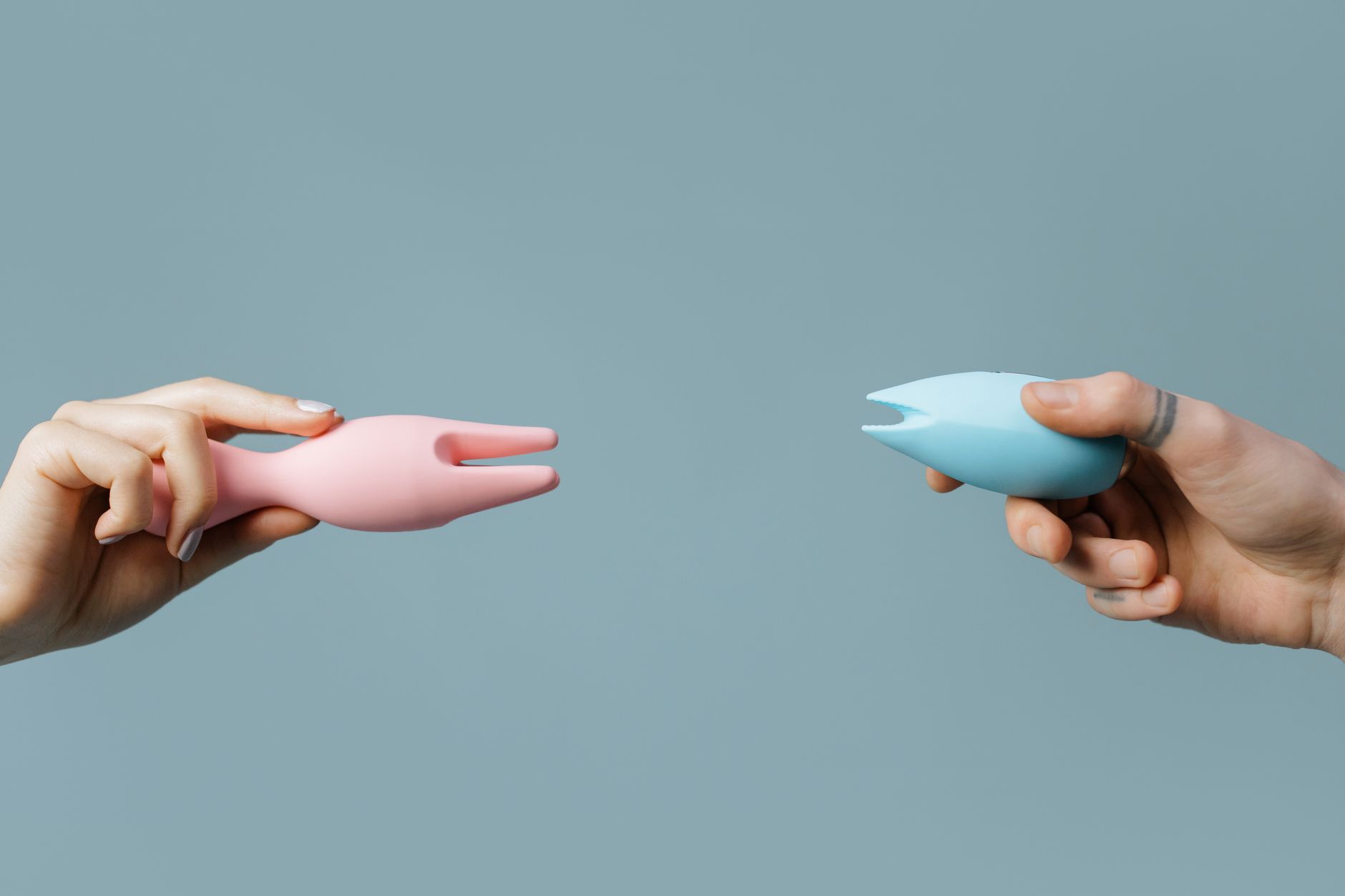 Due mani che tengono vibratori in silicone rosa e blu su sfondo pastello