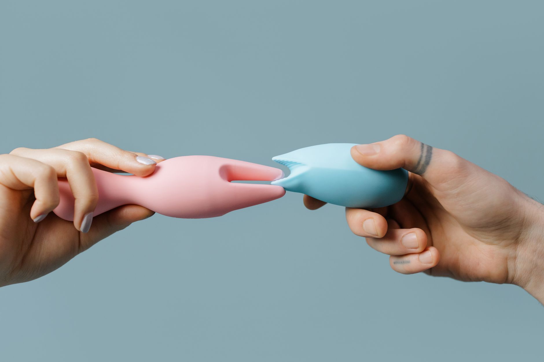 Mani che tengono un vibratore rosa e blu contro uno sfondo pastello