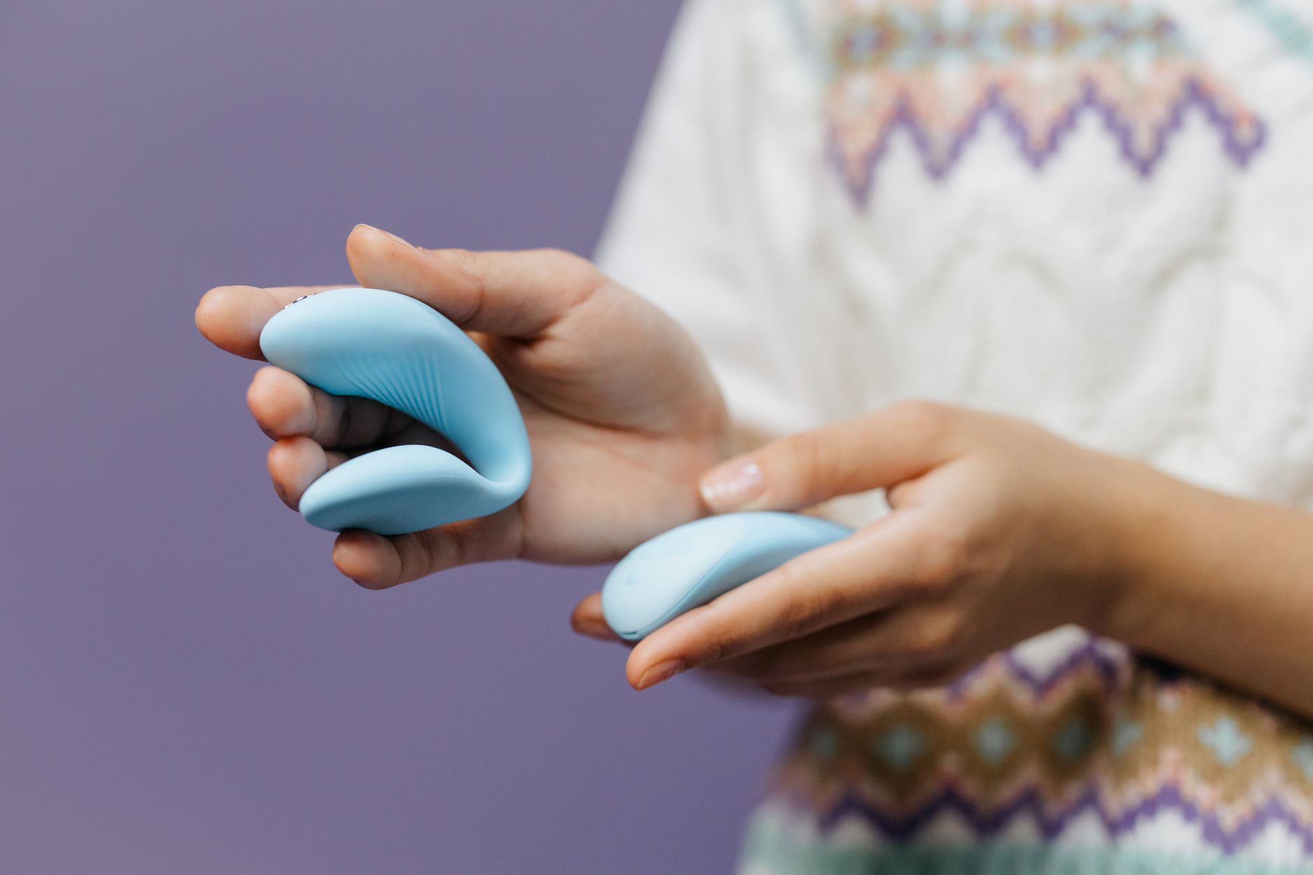 Mani che tengono un elegante vibratore blu contro uno sfondo viola, simbolo di intimità e piacere consapevole